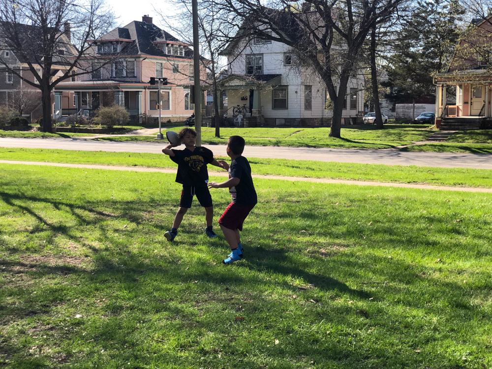 Two young boys toss a football in the grass