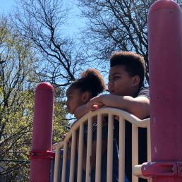 Two kids peer over the park equipment and observe park activity
